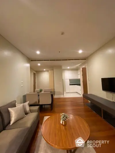 Spacious and modern living area seamlessly connected to a sleek kitchen, featuring warm wooden flooring and recessed lighting for a cozy ambiance.