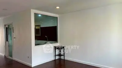 Minimalist interior with white walls and wooden flooring, featuring a small table and a window into another room.