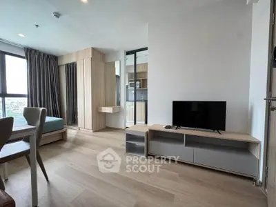 Modern living room with wooden flooring, TV stand, and large windows offering natural light.