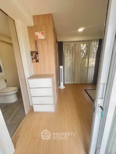 Spacious bedroom with wooden flooring and large window, featuring a modern bathroom and ample natural light.