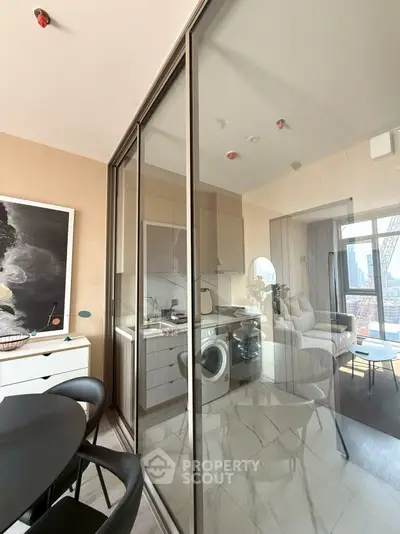 Modern apartment with glass-enclosed kitchen and city view, featuring sleek furniture and stylish decor.