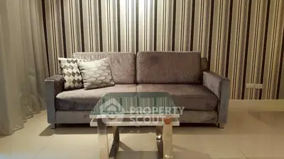 Stylish living room with modern sofa and glass coffee table, featuring elegant striped wallpaper.
