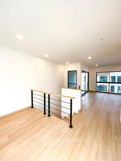 Spacious modern living room with wooden flooring and large windows for natural light.
