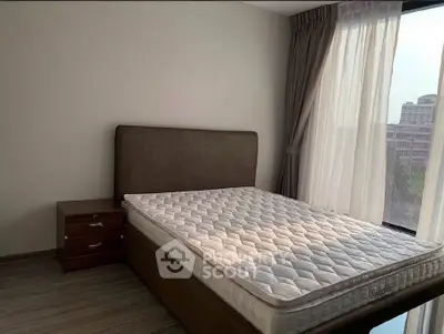 Spacious bedroom with large window and modern furnishings in a high-rise apartment.