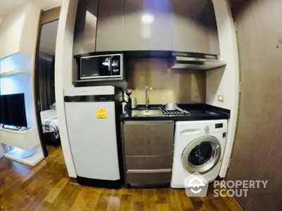 Modern compact kitchen with appliances including washing machine and microwave in stylish apartment.