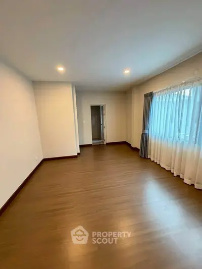 Spacious empty room with wooden flooring and large window, perfect for customization.