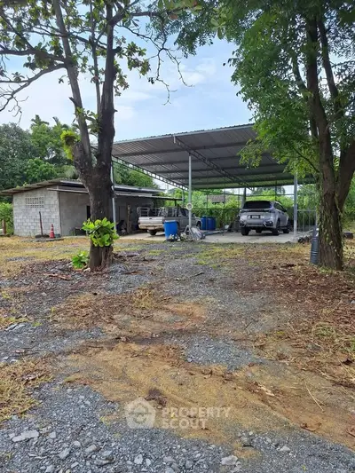 Spacious outdoor carport with metal roof and gravel driveway, surrounded by lush greenery.