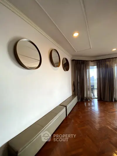Elegant living room with parquet flooring and stylish mirrors, offering a glimpse of a spacious balcony.