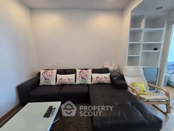 Modern living room with stylish black leather sofa and floral cushions, featuring a cozy reading nook.