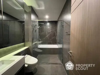 Sleek modern bathroom with dark stone tiles, glass shower enclosure, and elegant fixtures, perfect for a luxurious urban home.