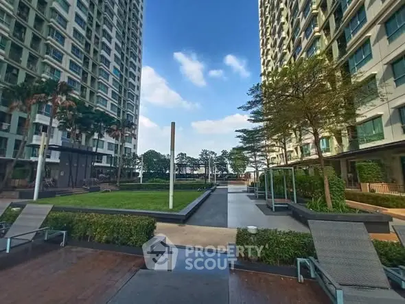 Modern residential complex with lush garden and high-rise buildings under blue sky.
