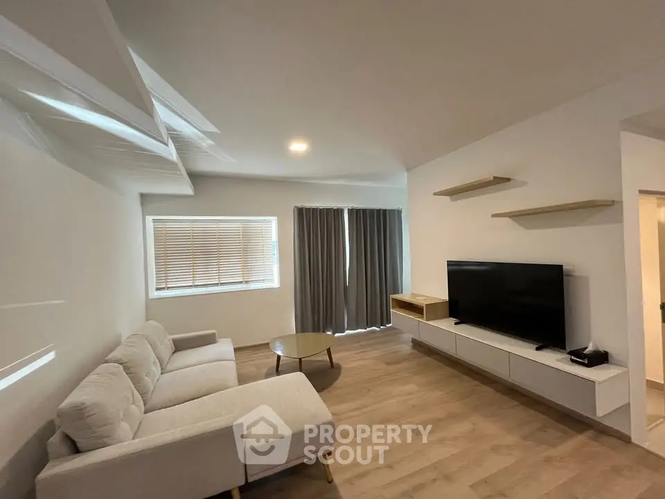 Modern living room with sleek furniture and wall-mounted TV, featuring natural light and minimalist design.