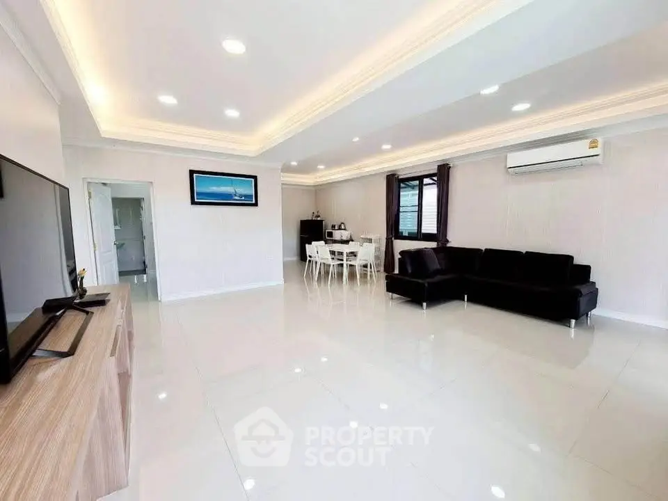 Spacious modern living room with sleek design and ample natural light, featuring a large black sofa and dining area.