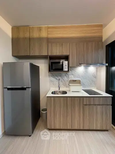 Modern kitchen with sleek cabinetry, stainless steel fridge, and built-in microwave in a stylish apartment.
