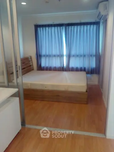 Cozy bedroom with wooden flooring and large window, perfect for relaxation.