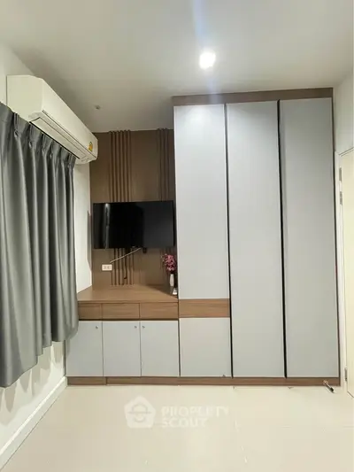 Modern bedroom with sleek wardrobe and wall-mounted TV, featuring minimalist design and neutral tones.