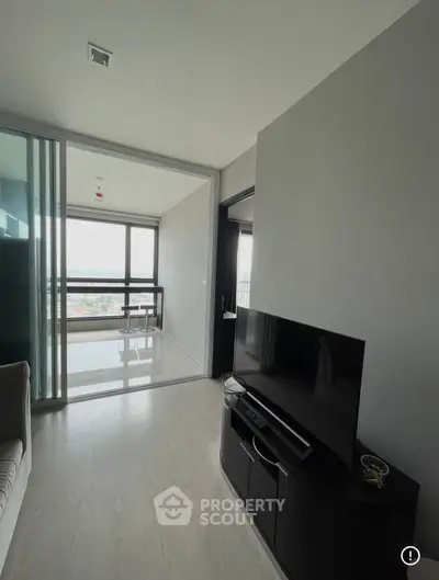 Modern living room with sleek TV setup and glass sliding doors leading to a bright balcony with city views.