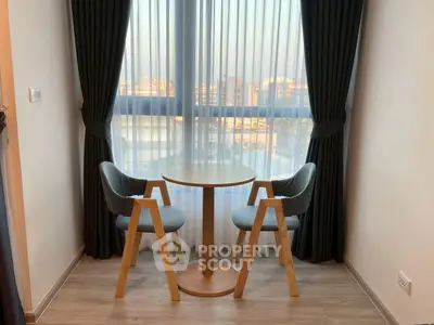 Cozy seating area with modern chairs and table by a large window with city view.