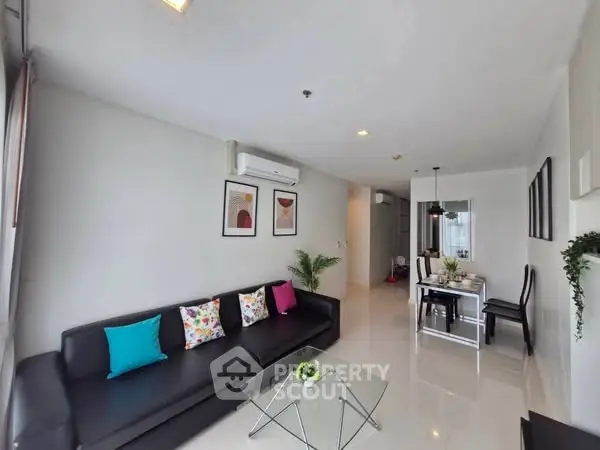 Modern living room with sleek black sofa and vibrant cushions, open layout dining area, and stylish decor.