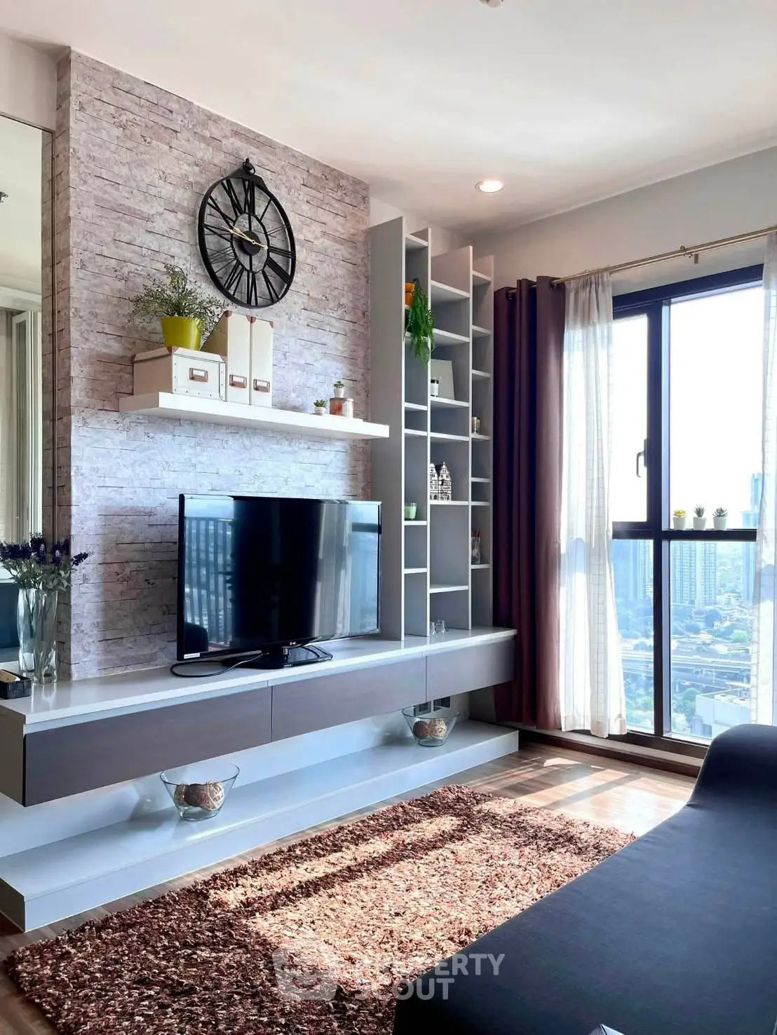 Modern living room with stylish decor and city view, featuring a sleek entertainment center and large window.