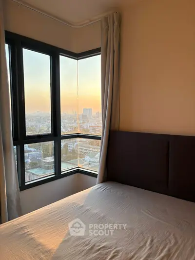 Cozy bedroom with stunning city view through large corner windows at sunset.