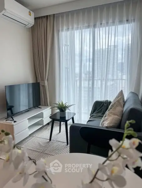 Modern living room with large window and city view, featuring cozy sofa and sleek TV setup.