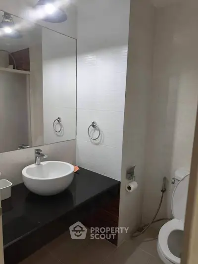 Modern bathroom with sleek black countertop and white basin, featuring a wall-mounted mirror and toilet.