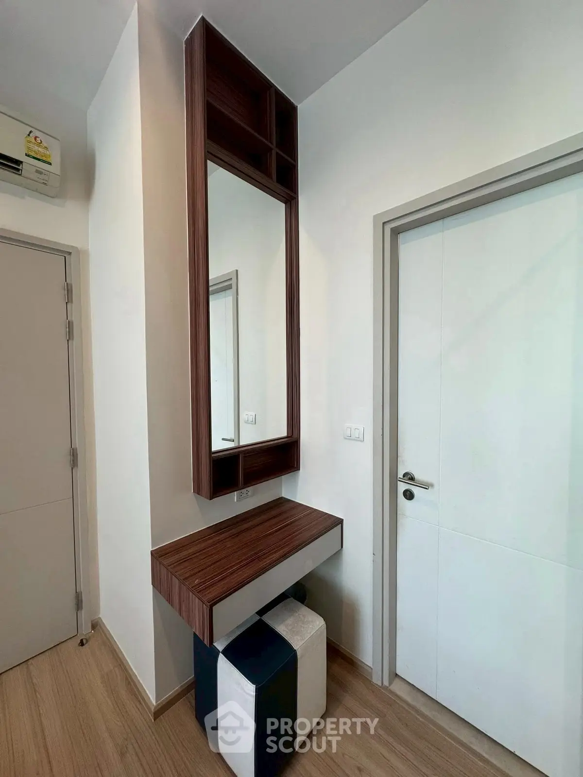 Modern minimalist vanity area with sleek wooden design and stool in a bright room.