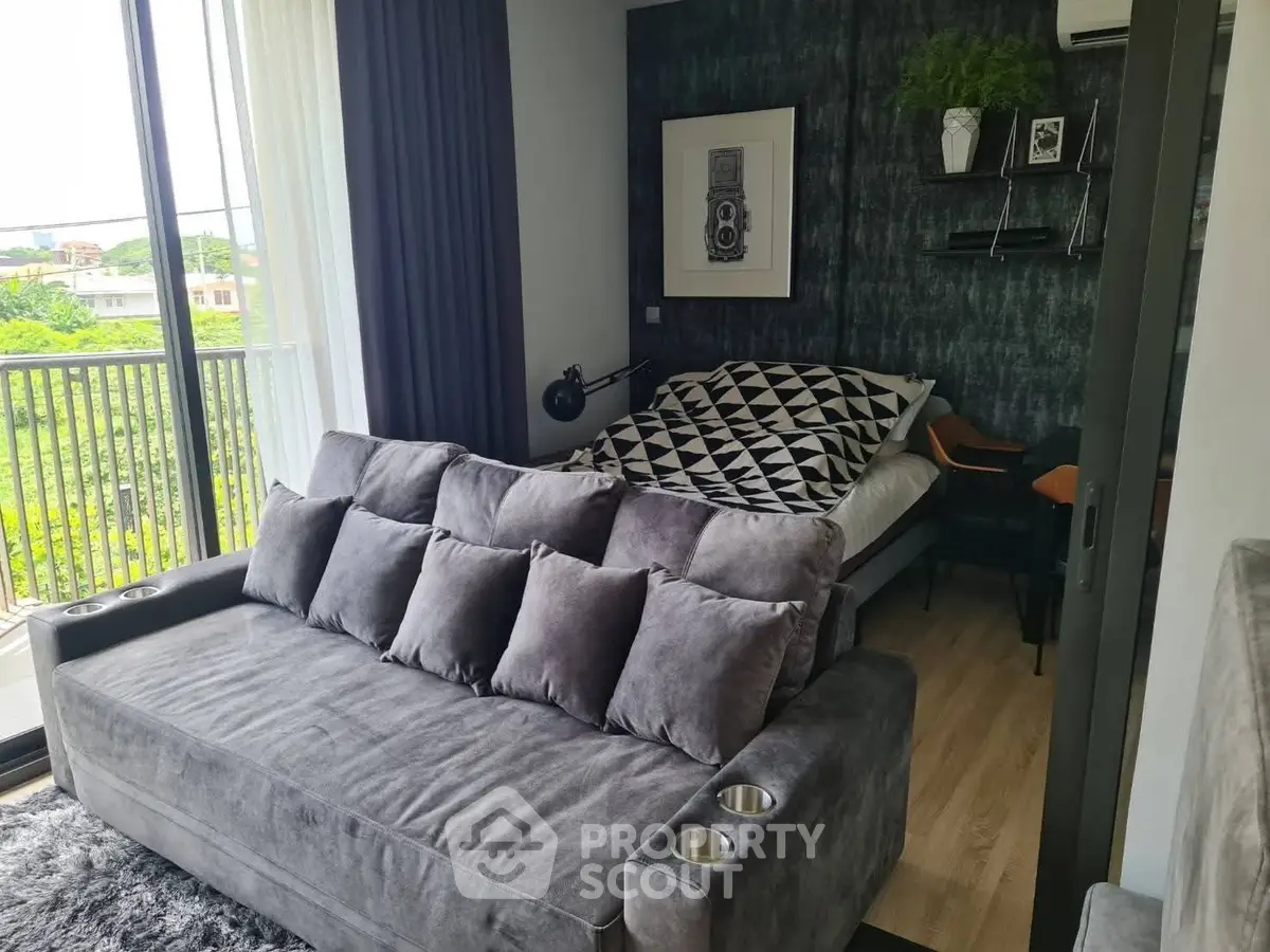 Stylish modern living room with plush gray sofa and cozy bedroom area, featuring a balcony view.