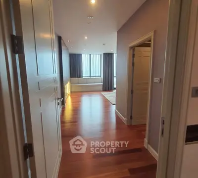 Spacious hallway leading to a bright living area with wooden flooring and large windows.