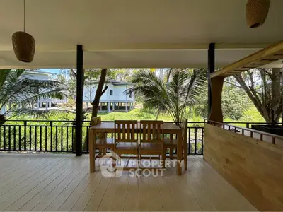 Spacious outdoor balcony with wooden furniture and lush greenery view, perfect for relaxation.