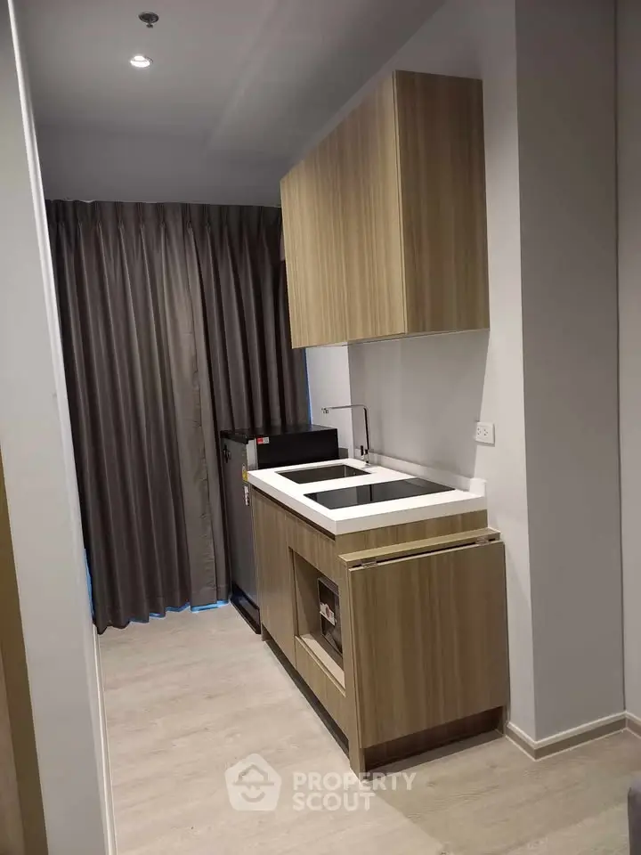 Modern compact kitchen with sleek wooden cabinets and integrated appliances in a stylish apartment.