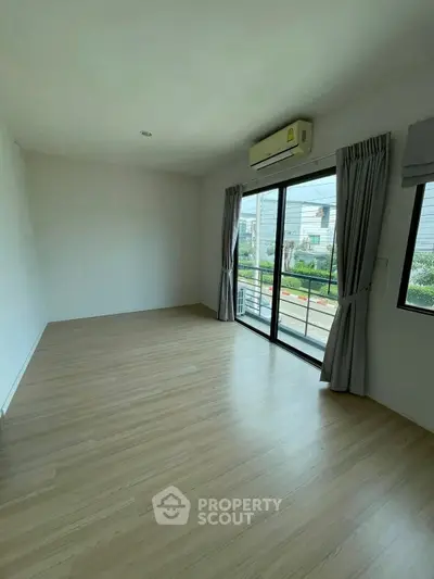 Spacious empty room with wooden flooring and large window leading to balcony.