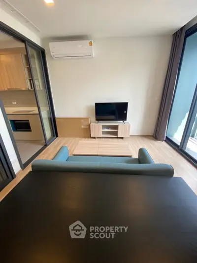 Modern living room with sleek furniture and open kitchen layout, featuring a cozy sofa and flat-screen TV.