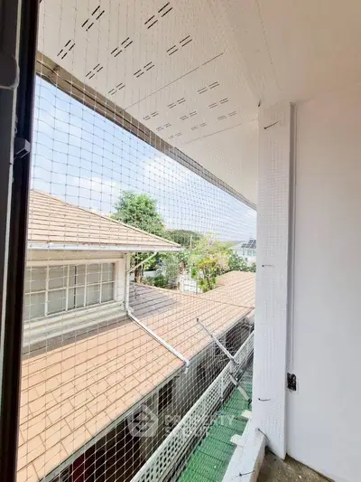 Charming balcony view with safety netting overlooking neighboring rooftops and greenery.