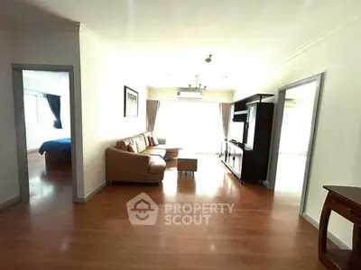 Spacious living room with wooden flooring and natural light, featuring a cozy sofa and entertainment unit.
