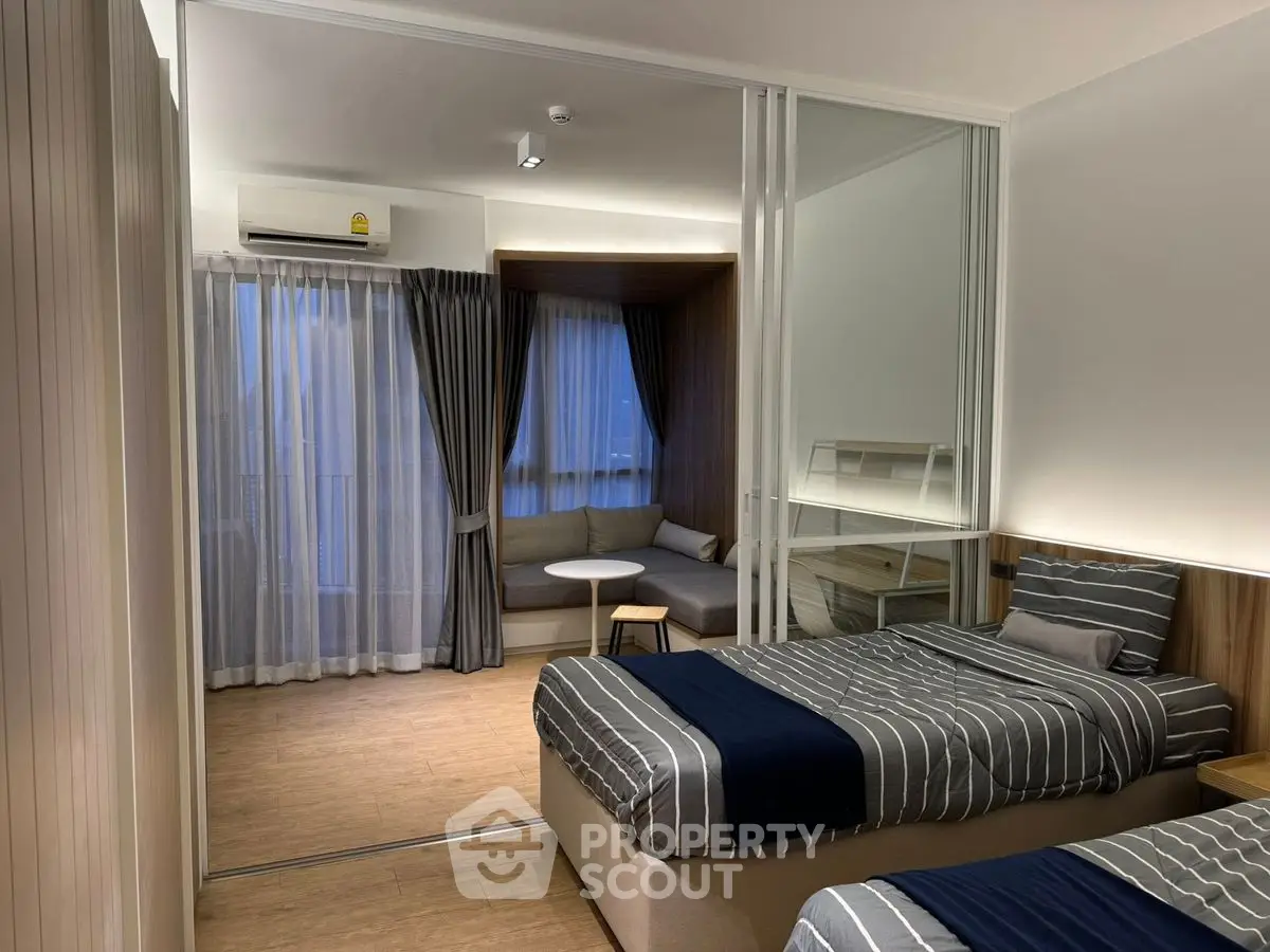 Modern bedroom with twin beds and cozy seating area, featuring sleek design and ambient lighting.