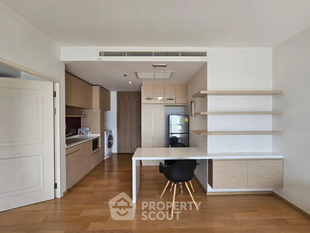 Modern kitchen with open layout and integrated dining area, featuring sleek cabinetry and wooden flooring.