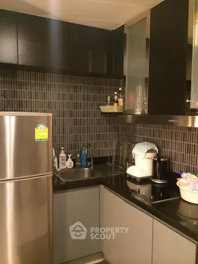 Modern kitchen with sleek cabinetry and stainless steel fridge in cozy apartment.