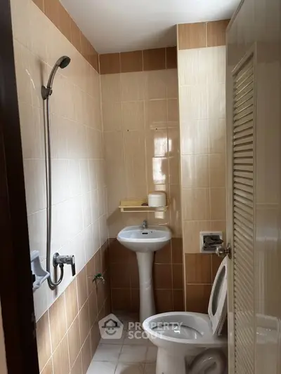 Compact bathroom with pedestal sink and wall-mounted shower in a cozy apartment.
