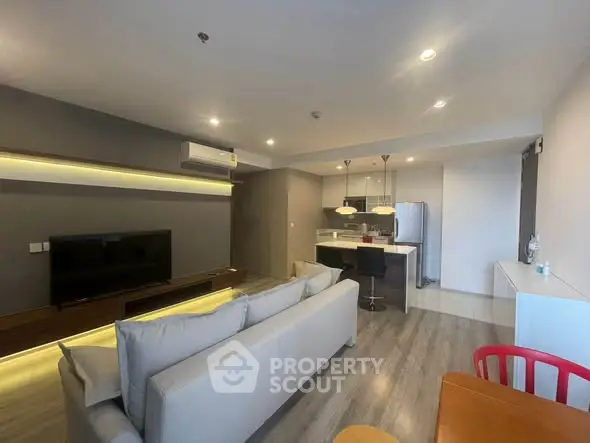 Modern living room with open kitchen, stylish lighting, and cozy seating area.