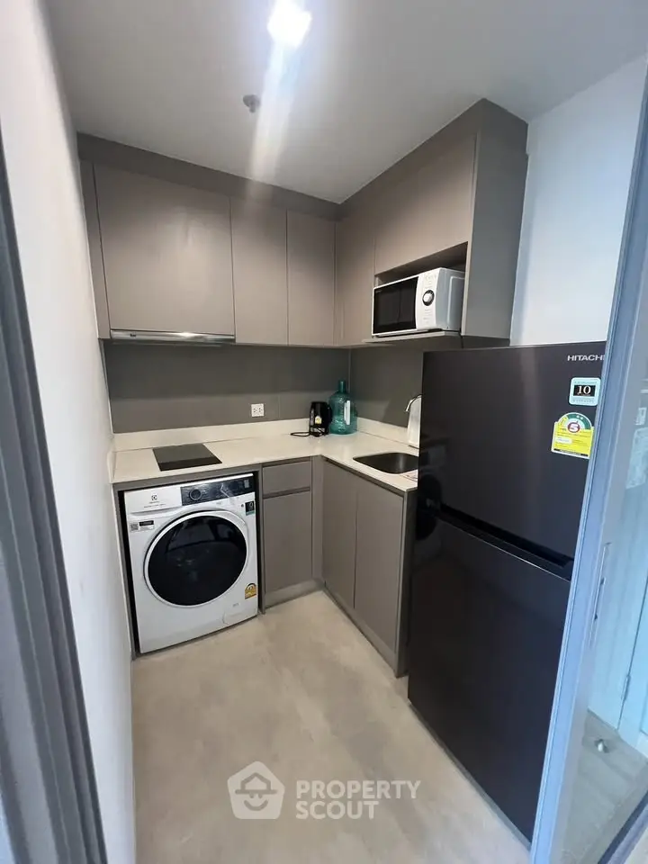 Modern compact kitchen with appliances including fridge, microwave, and washing machine in sleek design.