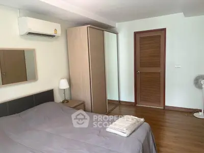 Cozy bedroom with wooden flooring, mirrored wardrobe, and air conditioning unit.