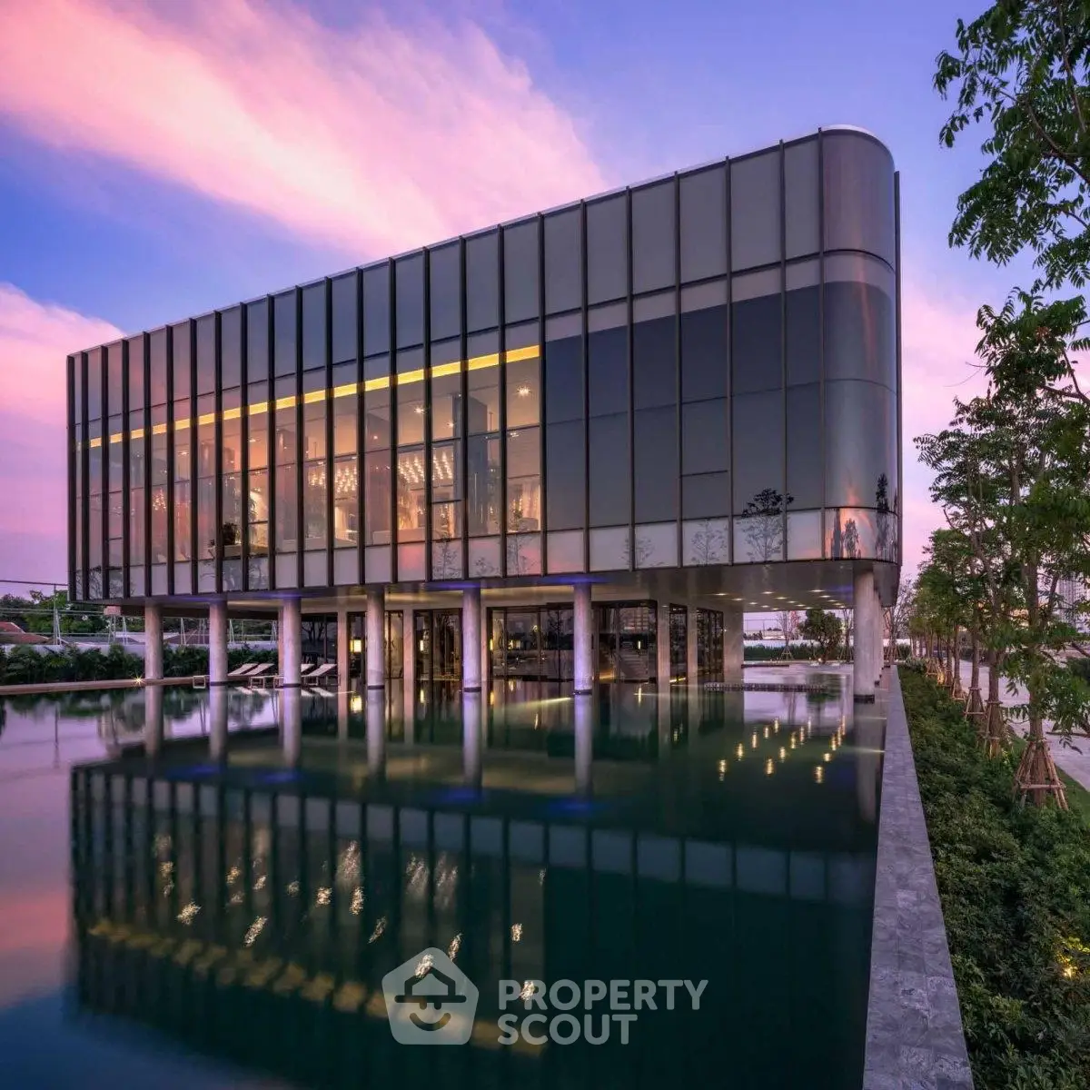 Stunning modern building with glass facade reflecting in tranquil water at sunset.