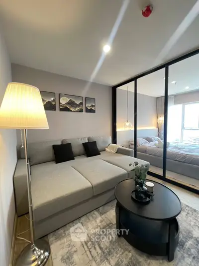 Modern living room with cozy sofa and stylish decor adjacent to a bedroom with glass partition.