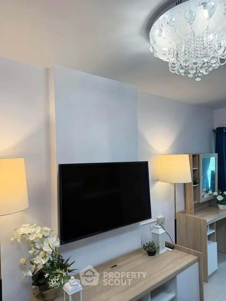 Modern living room with elegant chandelier and mounted TV, featuring stylish decor and ambient lighting.