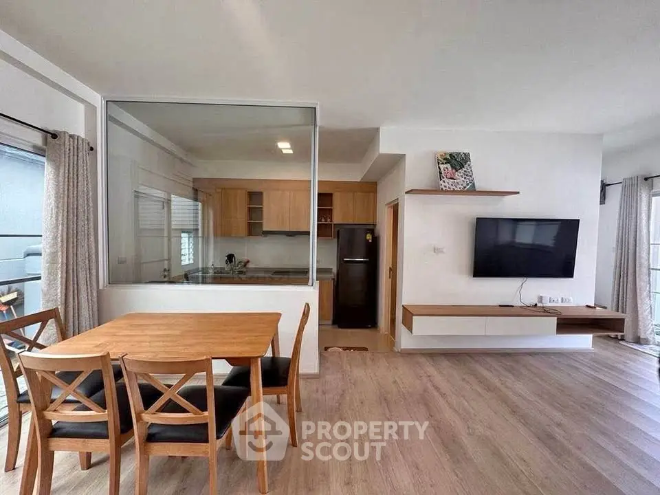 Modern open-plan living room with dining area and kitchen, featuring wooden flooring and contemporary furniture.