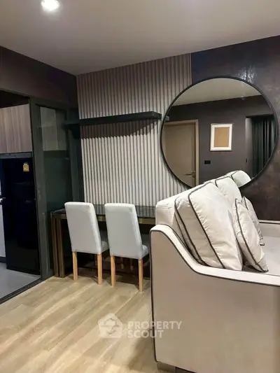 Modern living room with stylish decor and large round mirror, featuring a cozy seating area and elegant wooden flooring.