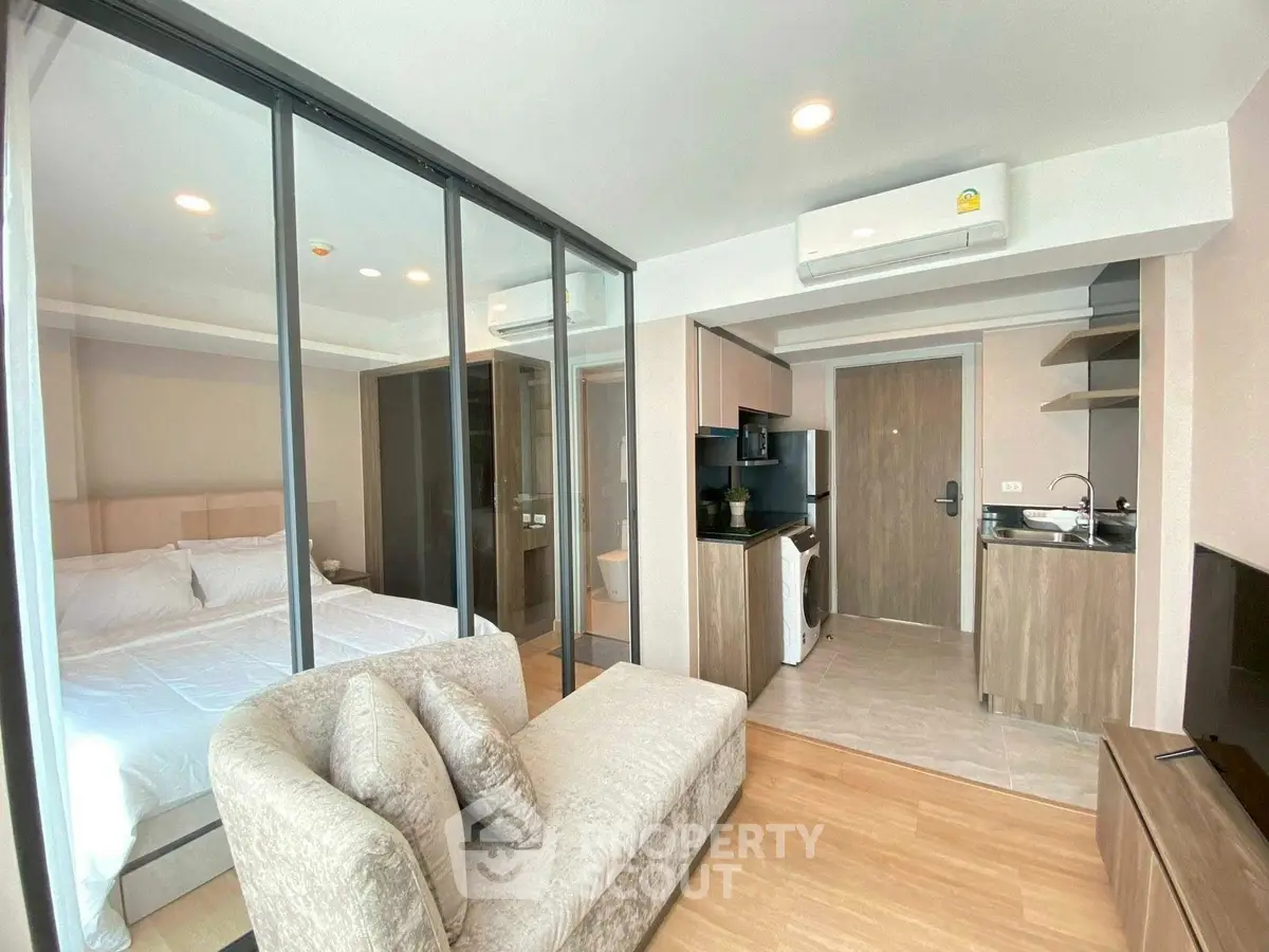 Modern studio apartment with glass partition, cozy sofa, and compact kitchen area.