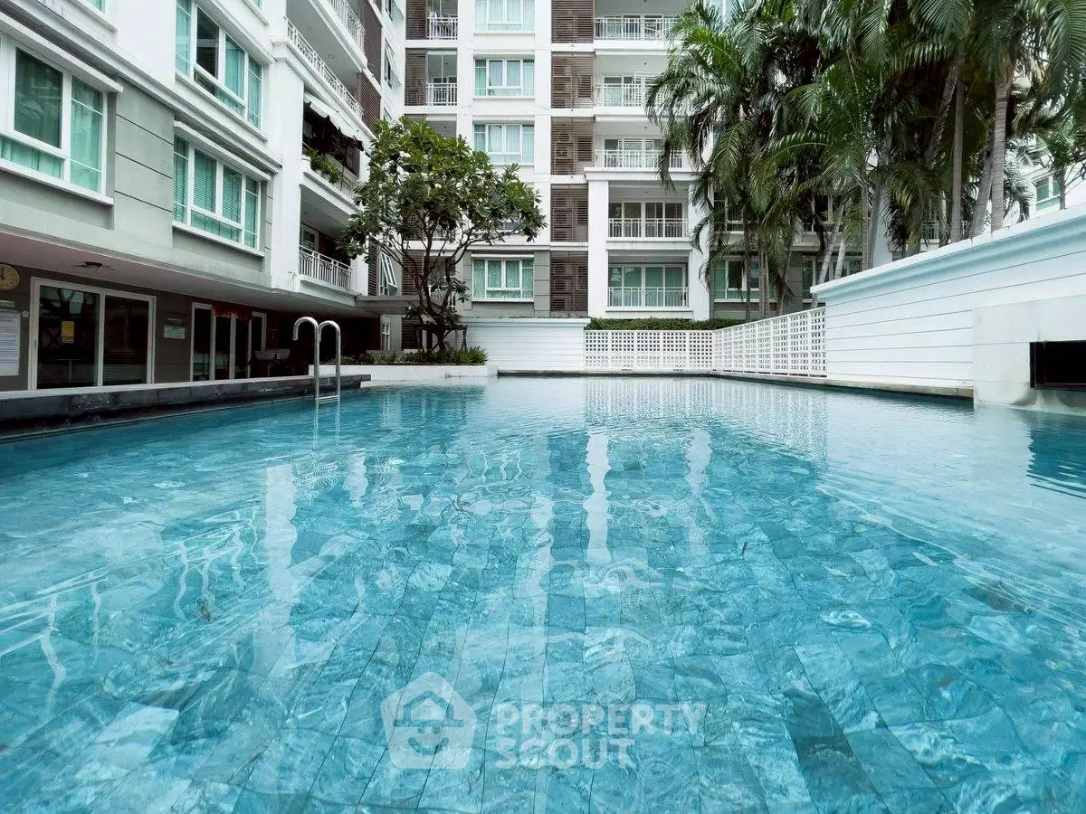 Luxurious residential pool area with modern building backdrop and lush greenery.